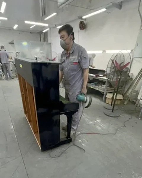 Technician polishing the case of a black upright piano with an orbital polisher