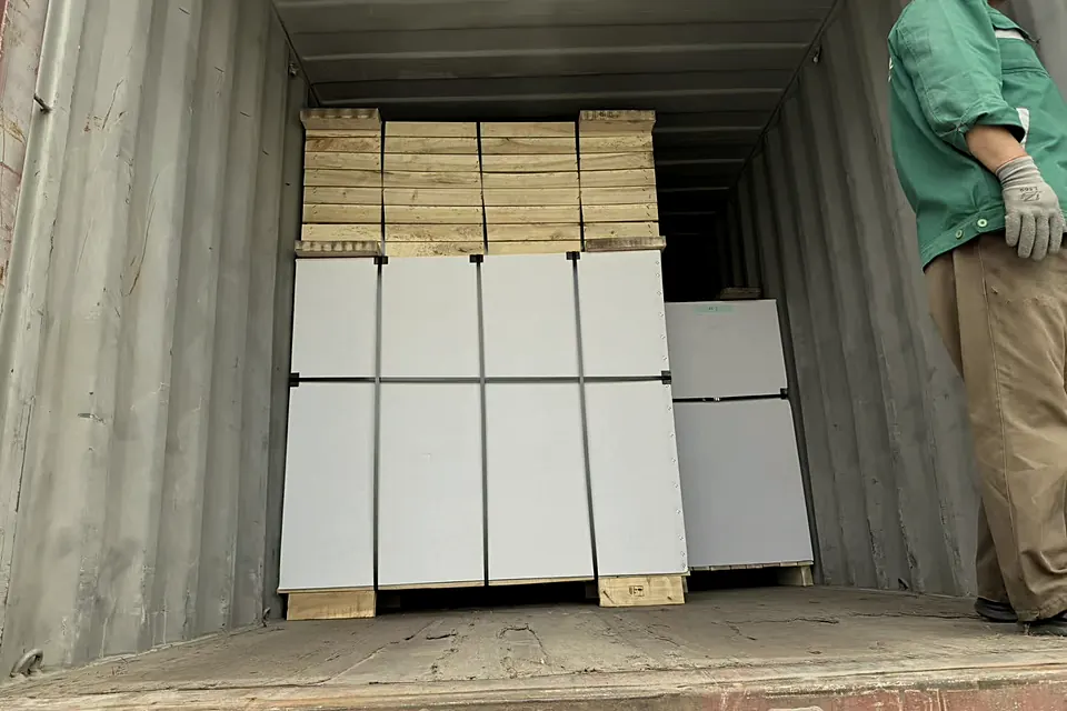 Packed pianos inside a shipping container, a worker beside them