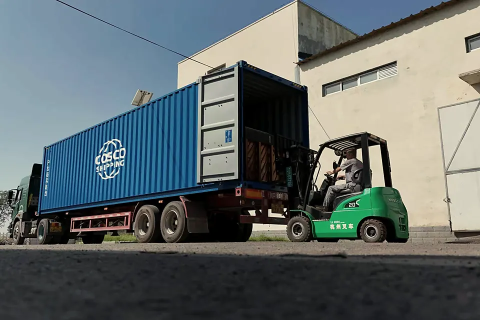 Forklift loading a blue shipping container on a truck