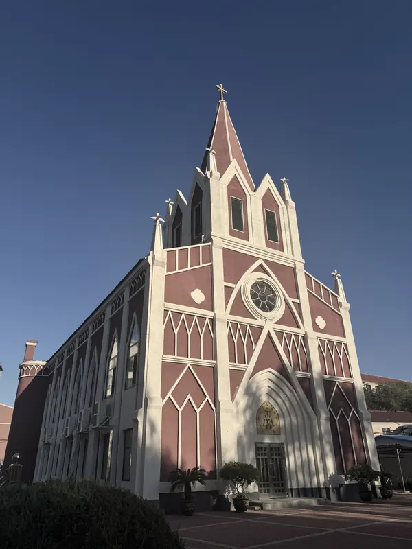 Yingkou Catholic Church, a red-and-white Gothic-style church with a tall spire, under a clear blue sky